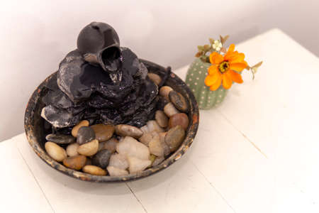 zen water fountian over a white background next to an orange flower in a small vase
