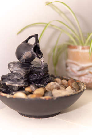 zen water fountian over a white background next to a green plant in a pot