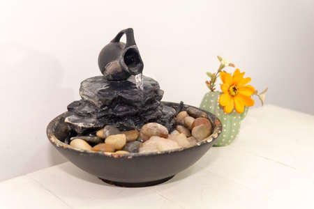 zen water fountian over a white background next to an orange flower in a small vase.の写真素材