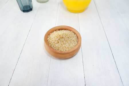 A bowl filled with uncooked white rice. On top of a white wood table