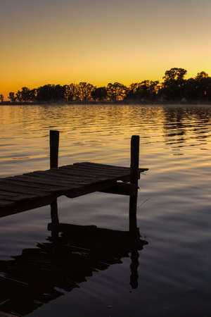 Sunset at Lobos lake, Buenos Aires. Taken from the shore looking to an old short wooden pier and the lakeの写真素材