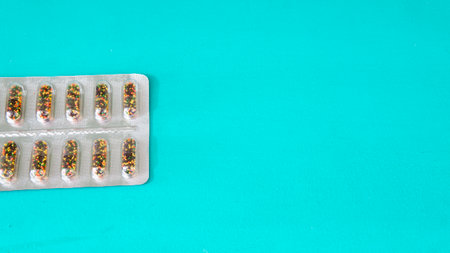 Flat lay view of a plastic blister with colorful pills placed on top of a cyan wooden surface with...