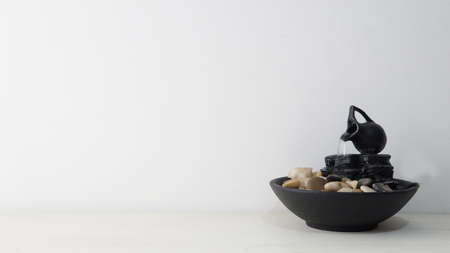 Close view of a zen water fountain over a white wooden table with a white backgroundの写真素材