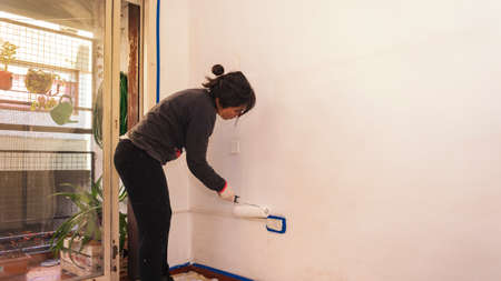Young lating woman painting a wall in her apartmentの写真素材