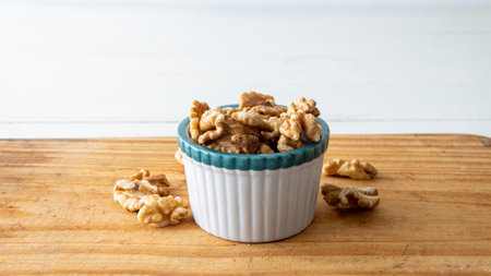close view of a small white creamy bowl loaded with walnuts. Placed on top of a wooden table with...