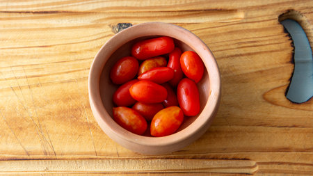 Close view of a bunch of fresh organic cherry tomatoes in a small bowl placed on a rustic wooden tableの写真素材