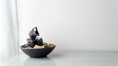 zen water fountain placed on top of a white wooden table next to a windowの写真素材