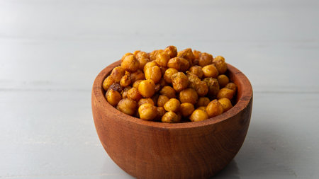 Close view of a wooden bowl filled with salty crispy chickpeas. over a white wooden tableの写真素材