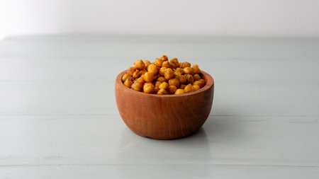 Close view of a wooden bowl filled with salty crispy chickpeas. over a white wooden tableの写真素材
