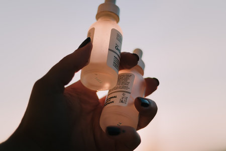 Female hand holding a bottle of serum oil in front of blurred backgroundの写真素材