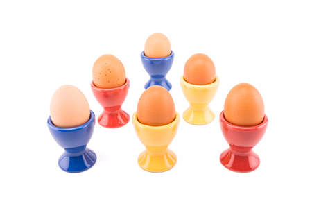 Six ceramic color egg cups with brown eggs.