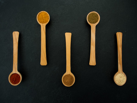Various spices in wooden spoon over black slate backgroundの写真素材