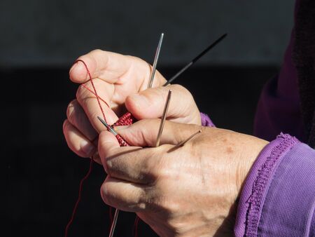Close up of senior woman's hands crocheting with red yarn