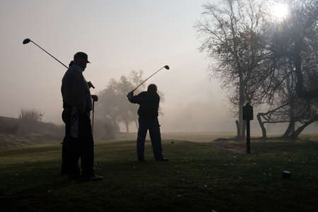 Early morning golfers silhouetted in a dense fog with a rising sunの写真素材