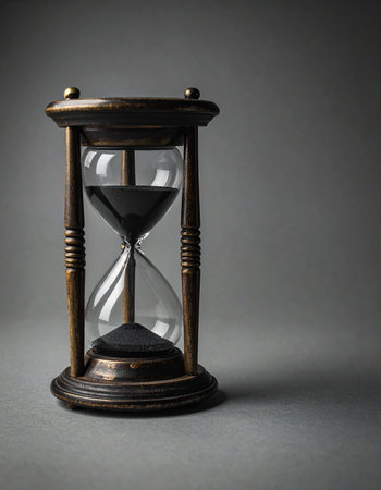 An elegant, vintage hourglass stands against a stark gray background. Black sand flows steadily, a silent and inexorable measure of passing moments. This classic instrument symbolizes deadlines, patience, and the finite nature of time, evoking a sense of contemplation and urgency.の素材