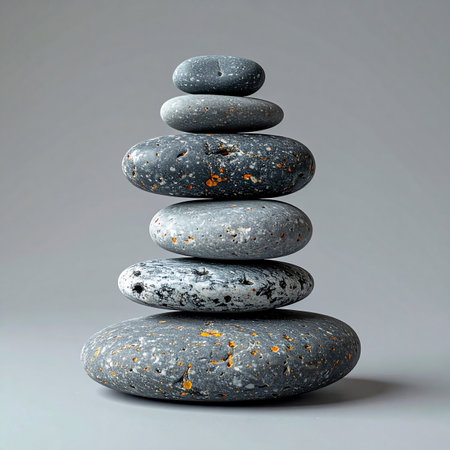 A carefully constructed tower of smooth, grey stones stands in perfect equilibrium against a neutral background. Each stone, unique in shape and texture, contributes to the overall sense of calm, stability, and mindful patience.の素材