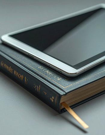 A sleek, modern tablet rests upon a classic hardcover book, symbolizing the evolution of knowledge and learning.の素材