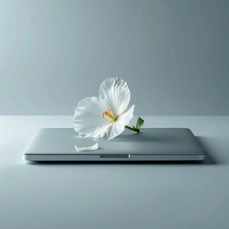 A single, delicate white flower rests on a sleek, closed laptop, symbolizing a harmonious balance between nature and modern technology.の素材