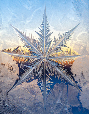 A perfect, star-shaped ice crystal forms on a cold windowpane, capturing the delicate and intricate beauty of winter.の素材