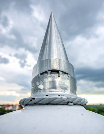A modern lightning rod stands as a silent guardian atop a building, its metallic spire pointing towards a dramatic, overcast sky.の素材