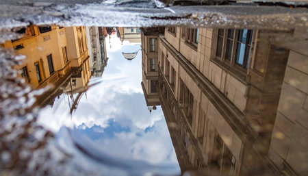 A city street reveals a hidden, upside-down world in the reflection of a puddle.の素材