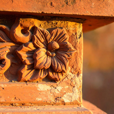 Golden sunlight catches the intricate details of a hand-carved floral motif on a weathered terracotta pillar.の素材