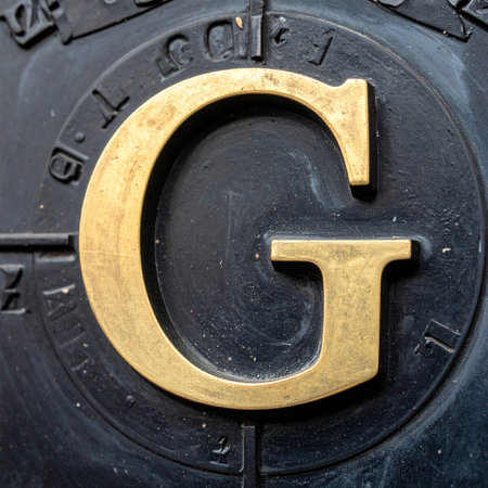 A close-up view of a bold, golden letter 'G' set against a dark, textured seal.の素材
