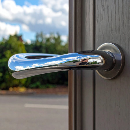 A close-up view of a sleek, polished chrome door handle on a modern front door.の素材