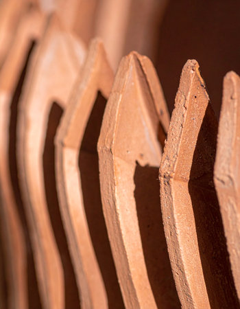 A close-up view captures the warm, earthy tones and repeating curves of terracotta roof tiles stacked in a neat row.の素材