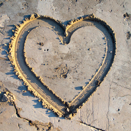 A heart, a universal symbol of love and affection, is carefully drawn into the wet, textured sand.の素材