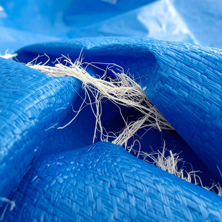 A close-up view reveals the stress and wear on a heavy-duty blue industrial tarp.の素材