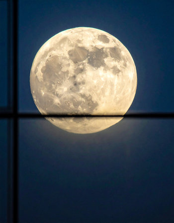 A brilliant full moon with detailed craters glows brightly in the deep blue night sky.の素材