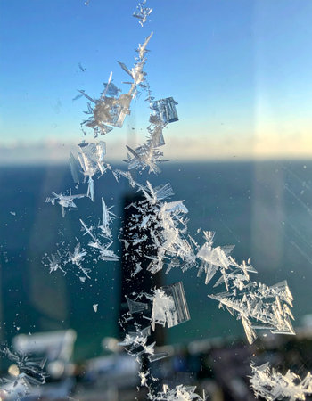 Intricate ice crystals bloom across a cold window pane, creating a delicate, frosty pattern.の素材