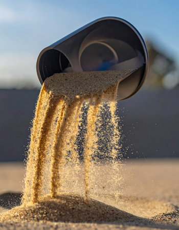 Golden grains of sand cascade from a dark scoop, captured in a moment of dynamic flow.の素材