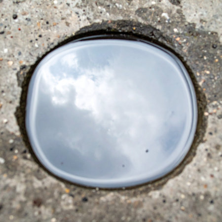 A small, forgotten puddle on a rough concrete surface becomes an unexpected window to the world above.の素材