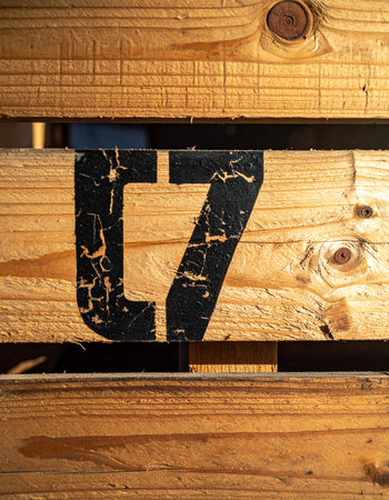 Close-up detail of the number seventeen stenciled in black on a rough wooden crate.の素材