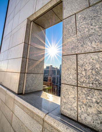 A brilliant sunburst shines through an opening in a modern stone building, casting a hopeful glow on the city beyond.の素材