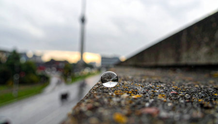 A single, perfect water droplet rests on a rough concrete surface, acting as a tiny crystal ball.の素材