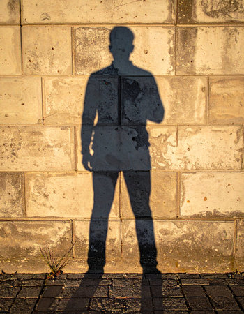 A silhouette of a person is cast upon a rough, textured wall, but this is no ordinary shadow.の素材