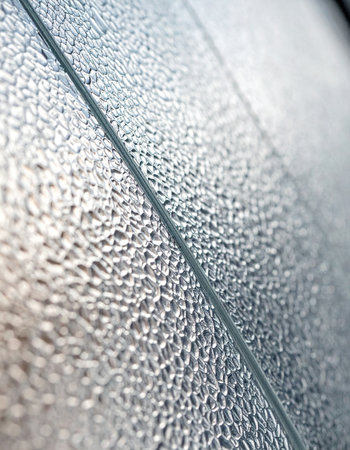 A close-up, angled perspective captures the intricate, pebbled texture of an obscure glass pane. A single diagonal line cuts across the frame, suggesting a division or boundary.の素材