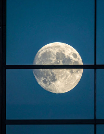 From the quiet comfort of a dark room, a large, detailed full moon hangs in the deep blue night sky.の素材