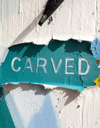 A close-up detail of a layered and weathered surface. The word 'CARVED' is embossed on a torn piece of green paper, creating a gritty, urban collage with a sense of history and permanence.の素材