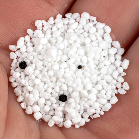 A macro shot captures a gardener's hand holding a precise mixture of white perlite and black fertilizer granules.の素材