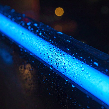 A vibrant blue neon light cuts through the darkness of a rainy night, its surface beaded with glistening raindrops.の素材