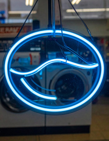 A vibrant blue neon sign glows brightly in the window of a city laundromat, its electric wave design promising clean clothes.の素材