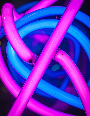 A chaotic tangle of vibrant pink and blue neon tubes glows intensely against a dark background.の素材