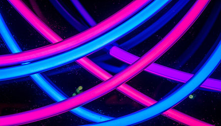Luminous tubes of neon pink and blue cross and overlap, creating an electrifying abstract pattern against a black background.の素材