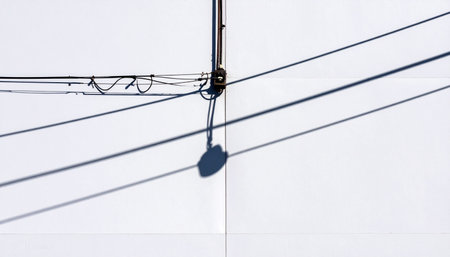 In a display of stark minimalism, electric power lines and their sharp shadows create a bold graphic pattern against a clean, white wall.の素材