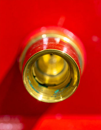 A macro, head-on view captures the precise engineering of a golden brass nozzle. Set against a bold, vibrant red background, the image highlights themes of industrial power, safety, and readiness.の素材
