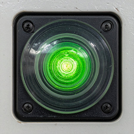 A vibrant green indicator light shines brightly from a control panel, signaling that a system is active, online, and ready.の素材